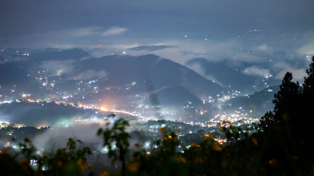 Dreamy night view long exposure photo of the Peradeniya city, Kandy, Sri Lanka from Hanthana mountain highlighting building lights & vehicle light trails surrounded by misty valleys between hills stock photo