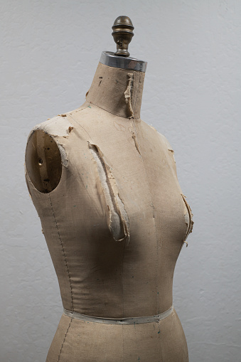 Old, very worn dress form for dressmaking, showing torso and hips - strong shadows and off-white natural background
