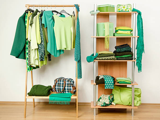 Dressing closet with green clothes arranged on hangers and shelf. stock photo
