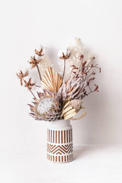Dried flower arrangement in a vase. Beautiful dried flower arrangement in a stylish ceramic white vase with brown aztec pattern. Dried flowers include pink proteas, banksia, gold palm leaf, kangaroo paw, cotton and ruscus leaves. dried plant photos stock pictures, royalty-free photos & images