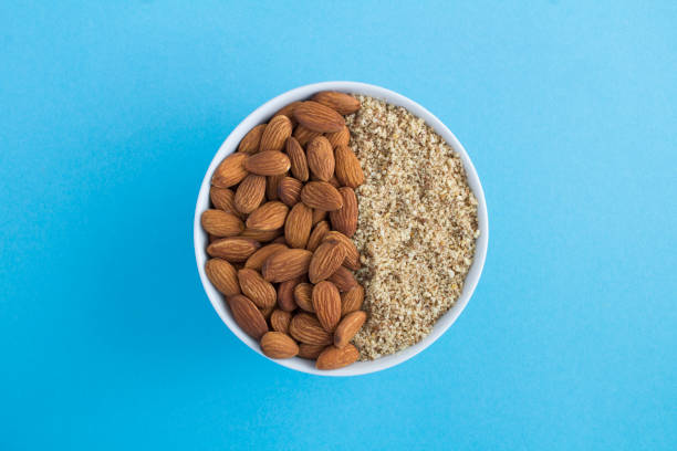 Dried whole and chopped almond in the white bowl on the blue background. Top view. Close-up. stock photo