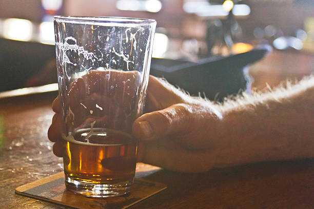 Drinking Beer At the Bar Close up of a man's hand grasping a mostly drunk, glass of beer with trails of suds on a bar coaster coaster stock pictures, royalty-free photos & images