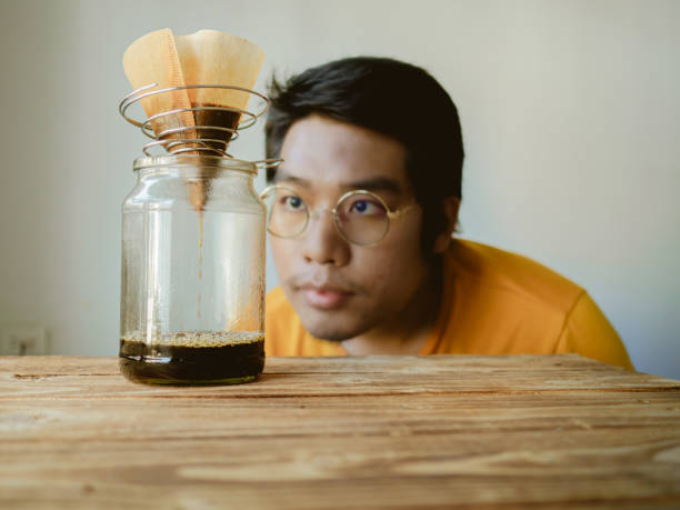 Drip brew by pouring hot water that has been filtered through roasted coffee beans contained in the filter.  man looking and observing the drip of coffee stock photo