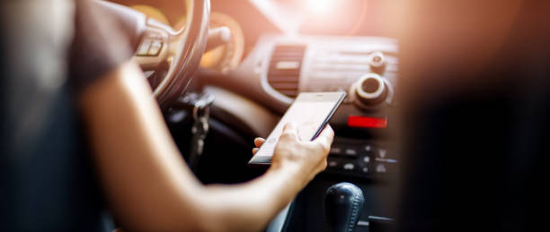 Driver driving a car on asphalt road in summer day at park. Driver driving a car on asphalt road in summer day at park. Woman at steering wheel with smartphone in her hand. distracted stock pictures, royalty-free photos & images