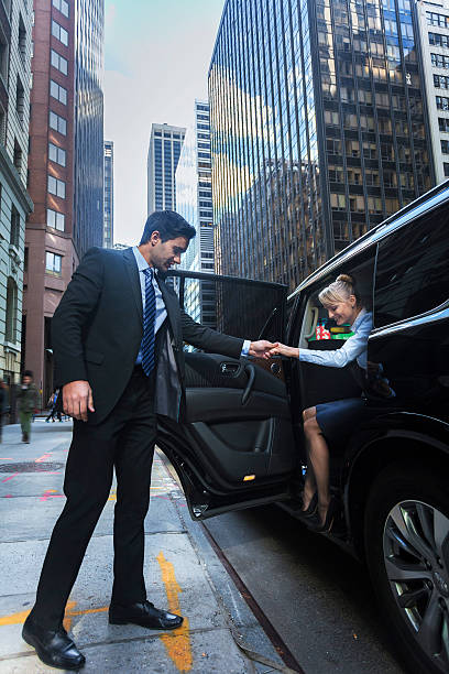 Driver helping passanger out of luxury car Young male driver helping a happy female passanger getting our of luxury black car in New York City open car door stock pictures, royalty-free photos & images