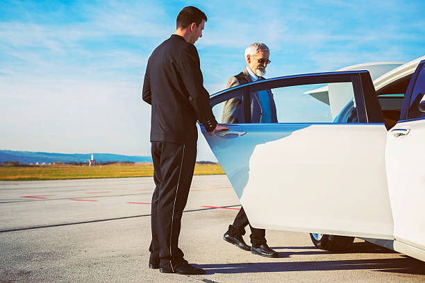 Driver helping senior adult into limousine at airport stock photo