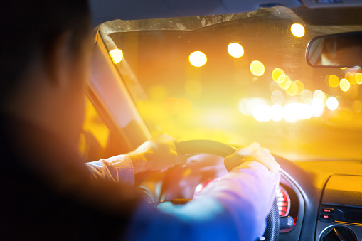Inside view of a man driving a car at night. Bright lights at background.