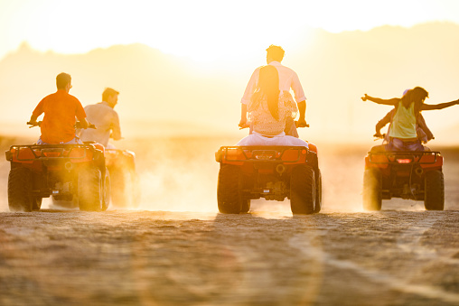 Back view of group of people driving quad bikes in the desert at sunset. Copy space.