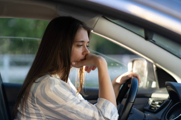 Drunk girl driving car. Unhappy tired young female in vehicle suffering from headache or handover stock photo