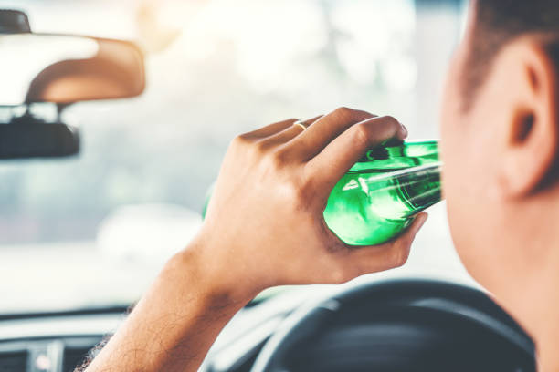 Drunk man driving a car on the road holding bottle beer Dangerous drunk driving concept stock photo