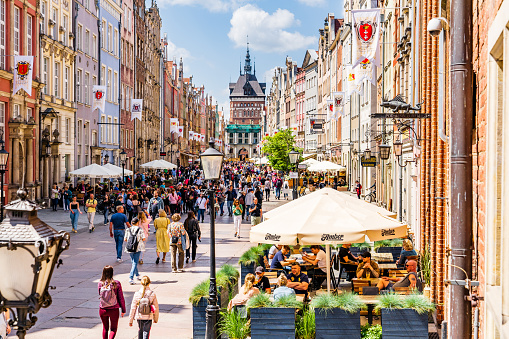 Old town of Gdansk, Srodmiescie historic district - crowds of tourists strolling along the Dluga street and chilling in cafes. The Golden Gate (Złota Brama) is on the background.