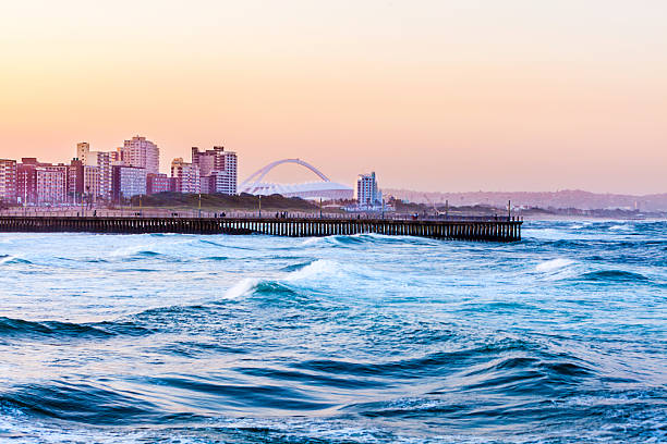 Durban seafront with world cup Stadium Durban evening sunset cityscape with stadium, Moses Mabhida Stadium, Kwazulu-Natal, South Africa, showing the pier on Durban beach. durban stock pictures, royalty-free photos & images