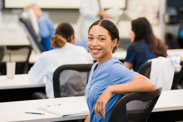 During patient care lecture, student turns to smile for camera During a lecture on patient care, the young adult female intern turns in her seat to smile for the camera. medical schools stock pictures, royalty-free photos & images