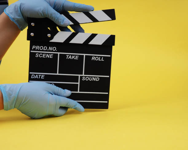 During the period of pandemics, hands in gloves concept of the film industry, a minimalistic composition on a yellow background with glasses and clapperboard. movies and cinema. stock photo