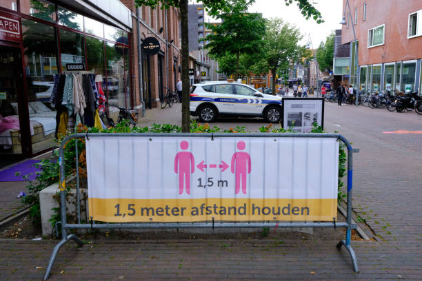 nederlands, houd je afstand veilig sociale distantiëren teken banner, shopping district. de achtergrond van de handhavingsauto - coronatest netherlands stockfoto's en -beelden