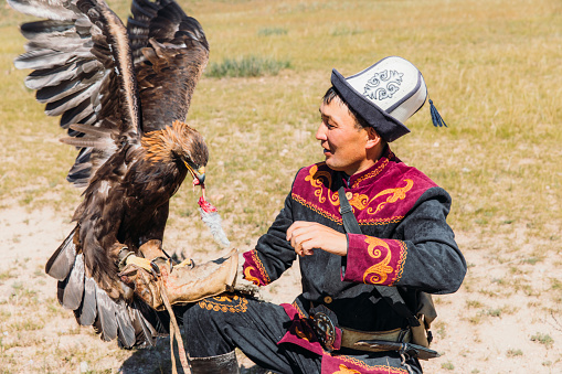 Portrait of a man hunter and his Eagle eating its prey -  an old tradition of eagle hunting in the wilderness area of Tian Shan mountains, Kyrgyzstan