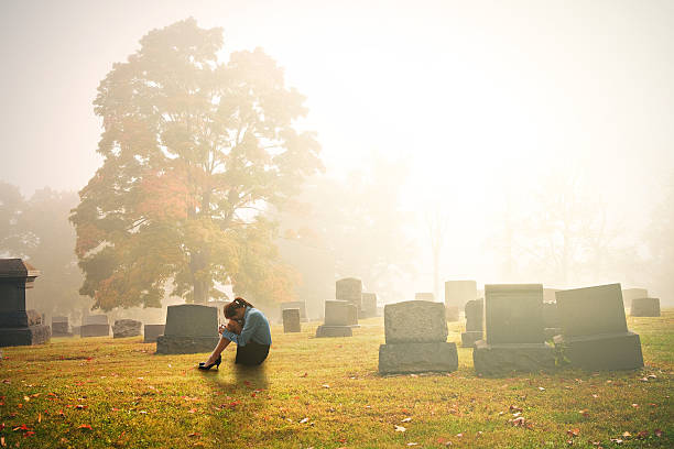 Early Mourning A woman in mourning sitting ina cemetery in the early morning. mourner stock pictures, royalty-free photos & images