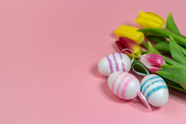 Easter border composition with Easter eggs and yellow and red tulips on a pink background. A stylish concept of minimalist decor. Space for copying. Festive flat banner with greeting card stock photo