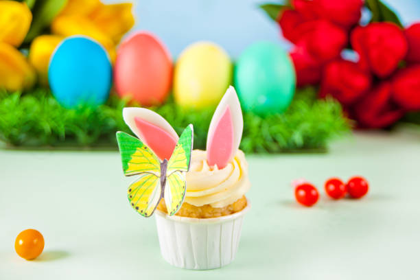 Easter funny bunny cupcake. Easter celebration festive table. Basket of flowers tulips on the background. stock photo