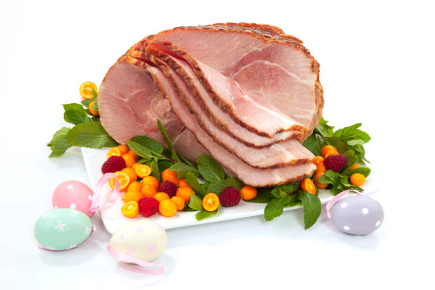 Easter Roasted Sliced Ham Closeup of delicious roasted sliced Easter ham with fresh mint, kumquat, and raspberries over white background. Easter eggs. ham stock pictures, royalty-free photos & images