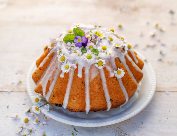 Easter yeast cake (Babka) covered with icing and decorated with edible flowers on a white plate on a white wooden table. stock photo