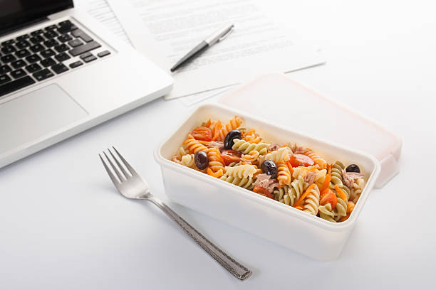 Eating a pasta salad in the office Eating a pasta salad with vegetables and tuna in the office plastic container stock pictures, royalty-free photos & images