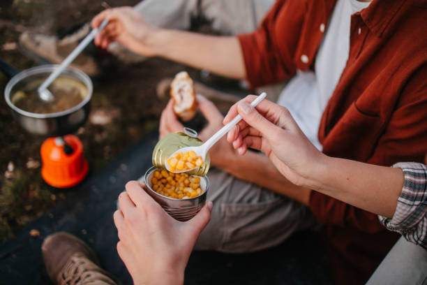 Eating during camping Campers eating sweetcorn from the can, making soup on a camping stove and holding a sandwich camping stove stock pictures, royalty-free photos & images
