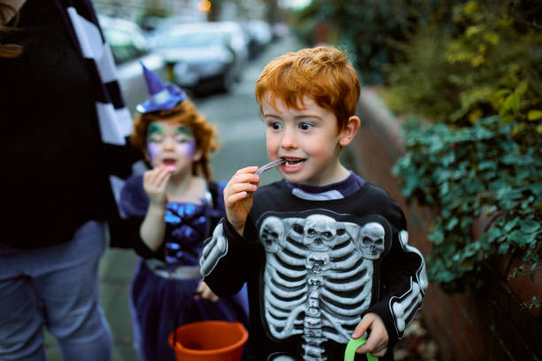 Eating Halloween Candy Little boy eating halloween candy while trick or treating in suburban streets with his mother and sister. sweet food photos stock pictures, royalty-free photos & images
