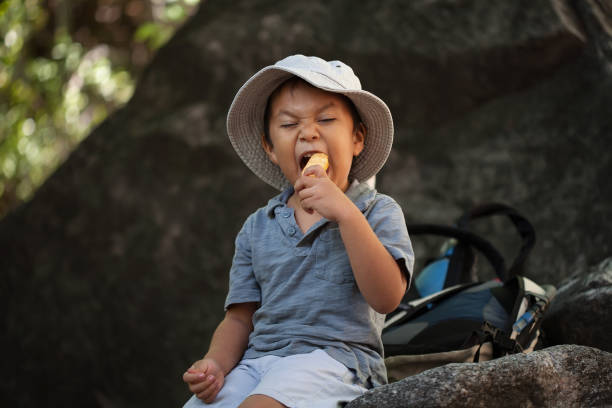 Eating healthy snacks, a young boy is taking a bite out of a apple while resting during a hike. stock photo
