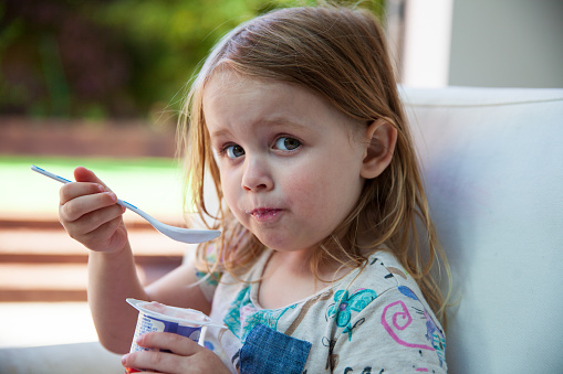 little girl eating yogurt with a big white spoon at home