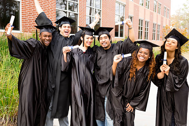 Education: Diverse group of friends excited after college graduation. Diplomas. Six, multi-ethnic friends dressed in black cap and gowns excitedly show off diplomas after college graduation. University school building background. 2015 photos stock pictures, royalty-free photos & images
