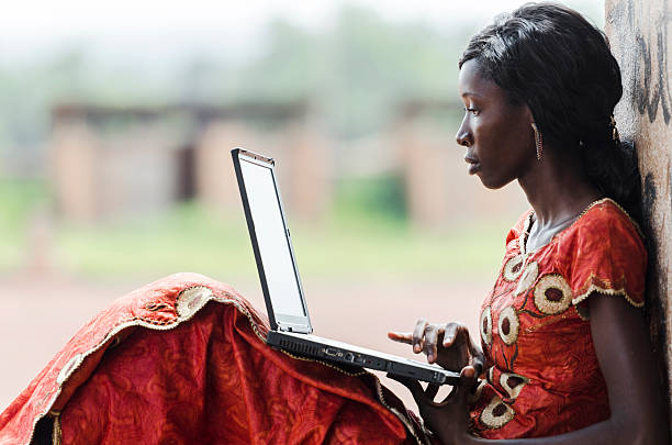 Education for Africa: Technology Symbol African Woman Studying Learning Lesson Street Shot of an African Ethnicity young woman working on business holding her technology item computer in a university in Bamako, Mali. Blurred background. University high school environment.  africa stock pictures, royalty-free photos & images