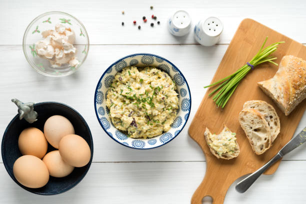 Egg salad in bowl topped with chives arranged on white table from above stock photo