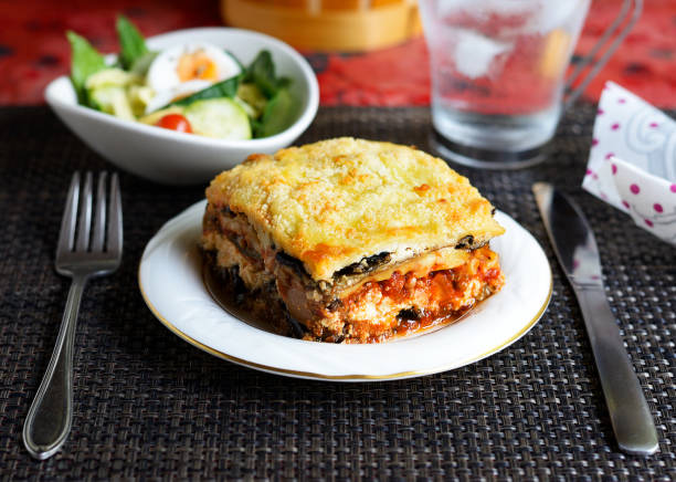 eggplant lasagna A piece of eggplant lasagna on a white dish with knife, fork, salad, and a glass of iced water. eggplant stock pictures, royalty-free photos & images