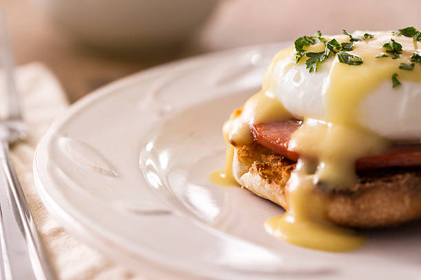 Eggs Benedict with Hollandaise Sauce Morning Breakfast - Eggs benedict with hollandaise sauce.  Eggs benedict is a dish made with a poached egg, ham, and toasted english muffin with hollandaise sauce on top.  Please see my portfolio for other food and drink images.  poached food photos stock pictures, royalty-free photos & images