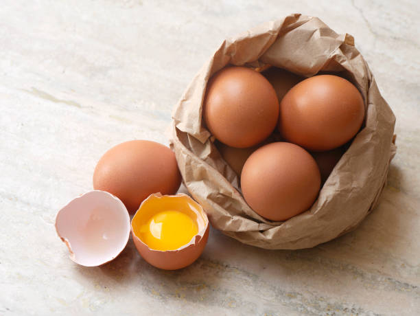 Eggs composition Eggs composition on marble surface, one of them is broken in two halves; some eggs are inside a paperbag. Natural day light horizontal composition with copy space, high angle view. No people. Color photography. egg yolk stock pictures, royalty-free photos & images