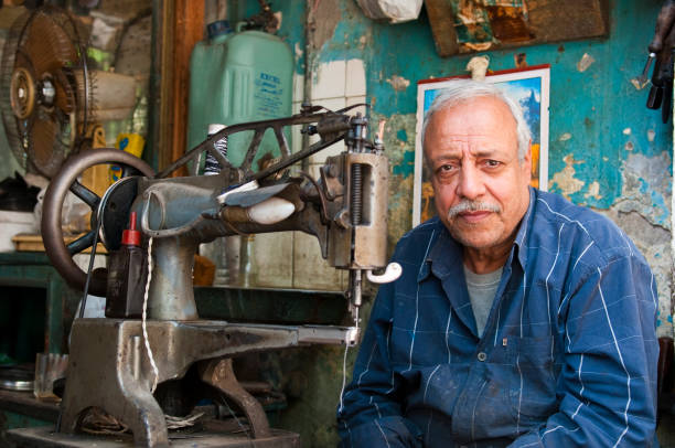 Egyptian man and sewing machine in Cairo, Egypt A Coptic Egyptian man, seen from the sidewalk outside his small shop, sits behind his sewing machine in Cairo, Egypt. coptic christianity stock pictures, royalty-free photos & images