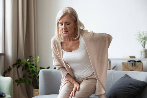 Elderly 60s woman suffer from back ache Elderly 60s woman got up from couch felt severe painful feelings in lumbar, massaging low back to reduce ache, suffer from backache discomfort, diseases of older people, sciatic nerve injury concept chronic illness stock pictures, royalty-free photos & images