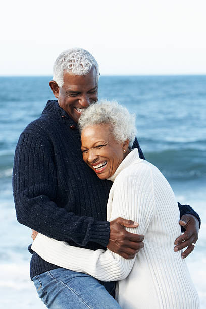 Elderly black couple hugging on beach Romantic Senior Couple Hugging On Beach By Sea Laughing old black couple in love stock pictures, royalty-free photos & images