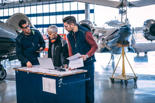 Elderly female aircraft engineer coordinating with her crew of mechanics in an airplane hangar Aircraft engineer crew coordinating together in an aircraft hangar. air vehicle stock pictures, royalty-free photos & images