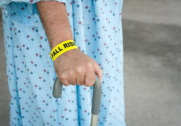 Elderly Man A Fall Risk An elderly man wearing a fall risk bracelet around his wrist at the hospital. Wearing a blue gown and walking with a cane. inpatient stock pictures, royalty-free photos & images