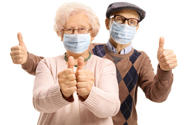 Elderly man and woman with protective face masks showing thumbs up stock photo