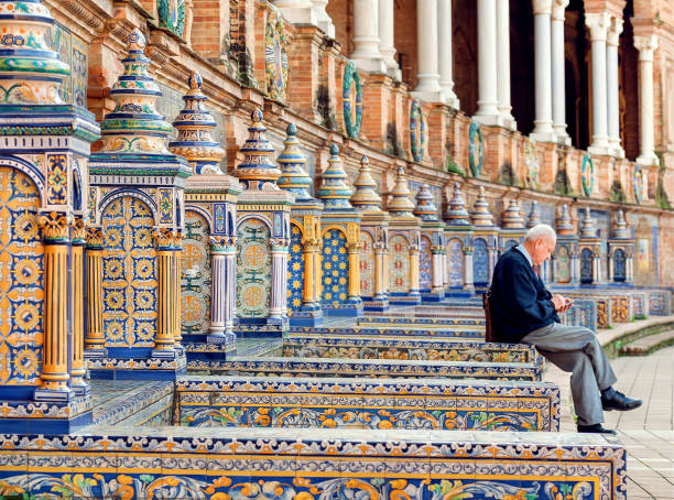 Elderly man sitting and relaxing on bench of famous Plaza de Espana, example of architecture of Andalusia stock photo