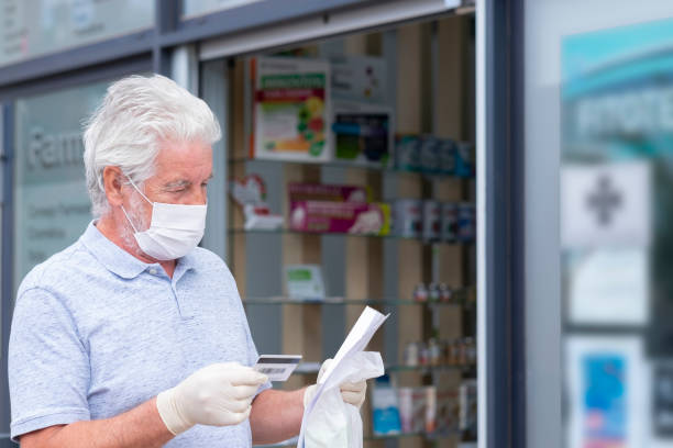 elderly man with mask and protective gloves leaves the chemist's shop with medicines and instructions. fear of coronavirus infection, covid-19. concept of retired senior and fear of contagion - cargo canarias imagens e fotografias de stock