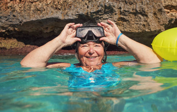 Elderly senior woman smiling in calm calm sea on sunny day, fixing her diving mask with hands, front view Elderly senior woman smiling in calm calm sea on sunny day, fixing her diving mask with hands, front view woman snorkeling stock pictures, royalty-free photos & images