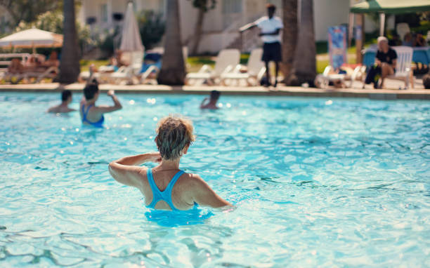 Elderly senior woman with grey hair, wearing blue swimsuit doing water aerobics in hotel pool, view from behind stock photo
