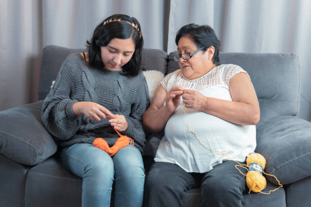 elderly woman 60 year old Latin grandmother knitting happily and comfortably inside her home and teaches her granddaughter manual activity stock photo