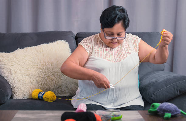 elderly woman 60 year old latin grandmother knitting happy and comfortable inside her home stock photo