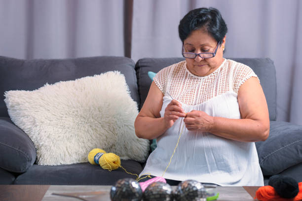 elderly woman 60 year old latin grandmother knitting happy and comfortable inside her home stock photo