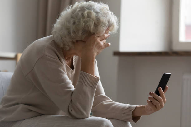 Elderly woman hold smartphone feels disappointed by received bad news Sad elderly woman sit on sofa hold smartphone feels disappointed by received sms bad news, awful message, difficulties with modern device usage, unpleasant notification, stressed older person concept white collar crime stock pictures, royalty-free photos & images